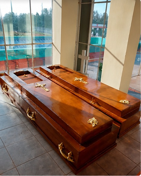Polished light-brown wooden coffins with gold crucifix and handles, displayed by the chapel windows