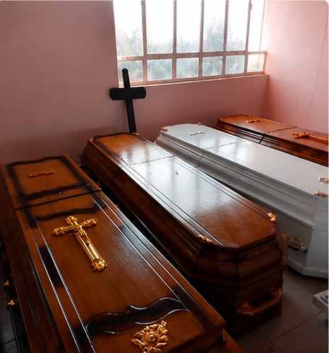Dark timber and white coffins displayed side by side beneath a wooden cross